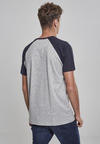 Grå och marinblå kortärmad T-shirt med raglan-design; mjukt tyg och rund halsringning. Synlig sömnad vid axlarna.
