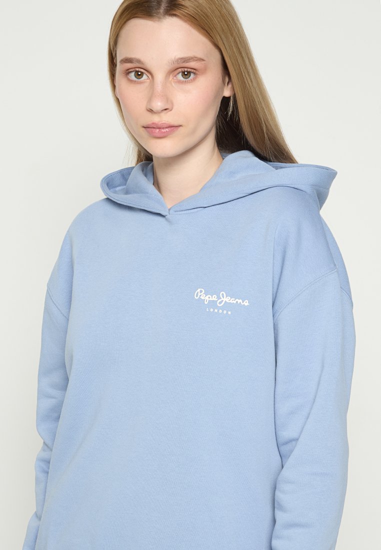 Jasnoniebieska bluza z kapturem, wykonana z miękkiego materiału, z dużym kapturem, obniżonymi ramionami i białym logo na piersi. Teksturowany, luźny krój.