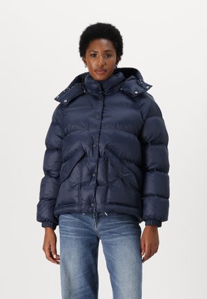 Veste matelassée bleu marine avec un col haut, des boutons pression et deux poches avant. Présente une texture matelassée et une conception ajustée à la taille.