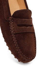 Mocassino in camoscio marrone con cinturino penny, cuciture dettagliate e suola in gomma con borchiette visibile su sfondo bianco.