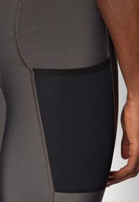 Szare legginsy sportowe z teksturowanym czarnym bocznym kieszonką, kontrastowym ściegem oraz eleganckim, dopasowanym krojem.