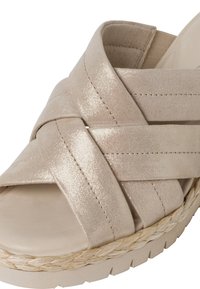 Sandale compensée beige avec larges brides croisées, semelle intérieure rembourrée et détail tressé le long du bord de la semelle.