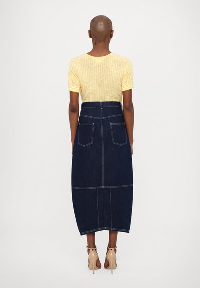 Gulstribet, kortærmet top parret med en mørk denim midi-nederdel, der har lommer og kontrasterende syninger, båret med nude højhælede sko.