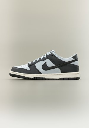 Nízkoprofilová Nike teniska v čiernej, bielej a šedej farbe so šnúrkami, perforovanou špičkou a logom Nike na boku a na päte.