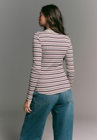 Långärmad randig skjorta med horisontella linjer i ljusbeige, röd och brun, tillverkad av ribbat material. Tillsammans med högmidjade denimjeans.