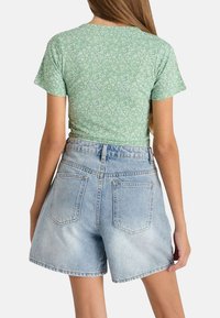 Haut floral vert à manches courtes associé à un short en denim bleu clair taille haute, avec des poches arrière et une coupe décontractée.