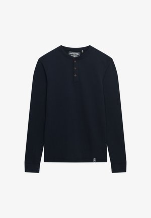 Granatowa koszula henley z długim rękawem, wykonana z miękkiej bawełny, z trzema brązowymi guzikami przy kołnierzyku i małą metką z logo na dole.