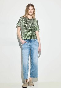 Zeleno-bíle pruhovaný top s krátkým rukávem, široké džíny v denimové modři a hnědé slip-on boty. Hladká bavlněná textura s volným střihem.