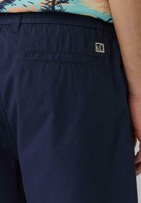 Siniset shortsit kevyestä kankaasta, joissa on takatasku ja pieni logo-ominaisuus. Sujuva pinta, joustavyysvyötärö näkyvissä.