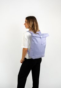 Lila, szövetből készült, sima tapintású roll-top hátizsák. Állítható pántokkal és oldalsó zsebekkel rendelkezik. Minimalista dizájn.