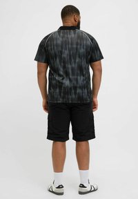 Polo de manga corta en negro con un patrón abstracto gris, con cuello negro y detalles blancos. Combinado con pantalones cortos cargo negros.