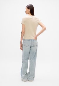 Beige kortermet t-skjorte med en tettsittende design, sammen med brede lyse blå denimbukser. Synlig søm og baklommer.