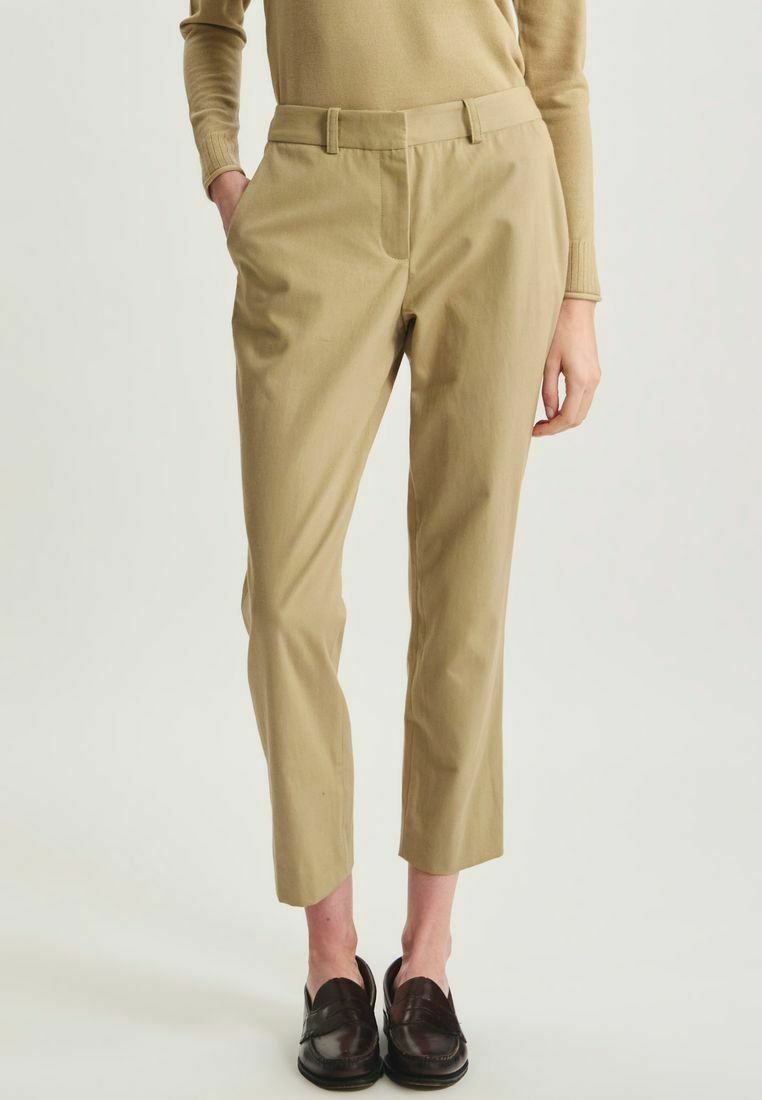 Pantalons en mélangé coton beige avec une coupe slim, des jambes fuselées, des passants de ceinture et des poches latérales. Texture lisse et design minimaliste.