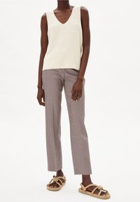 Vaalean kermaan vivahtava neulottu hihaton paita, jossa on V-pääntie, yhdistetty ruskeavalkoisiin ruudullisiin housuihin ja kerrostettuna ruskeilla, solmituilla sandaaleilla.