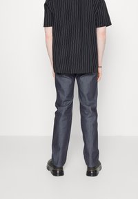 Svartrandig kortärmad skjorta som är parat med mörka denimbyxor och svarta skor. Tyget har en mjuk textur, och passformen är avslappnad.