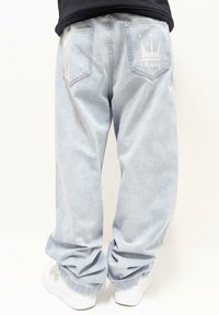 Gaiši zili plata džinsu bikses ar divām aizmugurējām kabatām, ar krona logo druku labajā kabatā. Saskaņotas ar baltām sporta kurpēm.