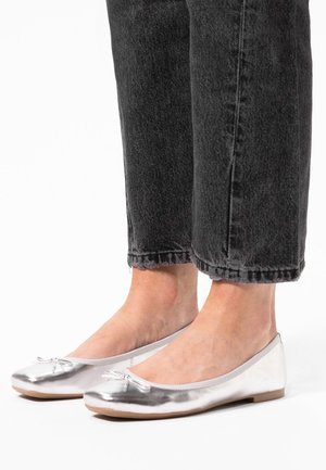 Zilveren balletschoenen met een metallic afwerking, ronde neuzen en een decoratieve strik. Gecombineerd met zwarte spijkerbroeken die op de enkels geknipt zijn.