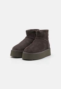 Bottines en daim marron avec un bout rond, une fermeture éclair sur le côté et une semelle plateforme épaisse et texturée de couleur verte. Détails de couture plate le long des coutures.