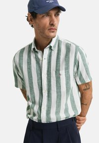 Camisa de lino de rayas verde y blanca de manga corta, con cuello abotonado y un bolsillo en el pecho con un detalle de logo.