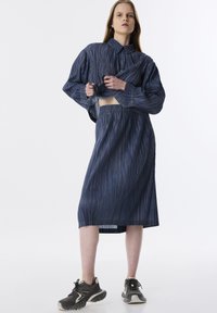 Conjunto de dos piezas de denim que incluye una camisa corta con botones y una falda de longitud media, ambas con rayas verticales en azul oscuro y costuras amarillas.