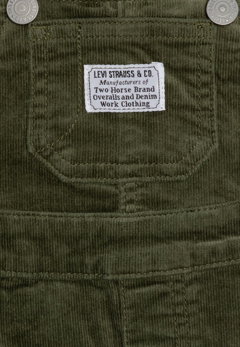 Tela de corduroy verde oliva con una superficie texturizada; incluye una etiqueta blanca que dice "Levi Strauss & Co." y acentos de hardware metálico.