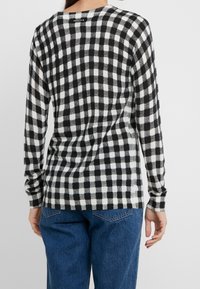 Langärmliges kariertes Hemd in Schwarz und Weiß aus einem weichen, strukturierten Stoff. Verfügt über einen runden Hals und ein tailliertes Design mit einem abgerundeten Saum.