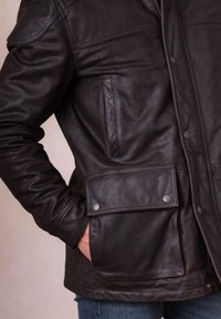 Dark brown leather jacket featuring a zippered front, side pockets, and a flap pocket with snap closures. Soft, textured finish and tailored fit.
