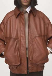 Brązowa skórzana kurtka o luźnym kroju, z kołnierzem, dwoma przednimi kieszeniami i ściągaczem w dole. Gładka faktura i suwak na dole.