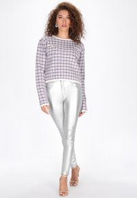 Lila és fehér kockás, hosszú ujjú pulóver, elülső zsebekkel, csillogó ezüst leggingssel és csupasz szandálmagassarkúval párosítva.