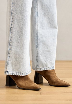 Braune Wildleder-Ankle-Boots mit spitzem Zehen, Blockabsatz und glatter Textur, kombiniert mit hellblauen weit geschnittenen Jeans.