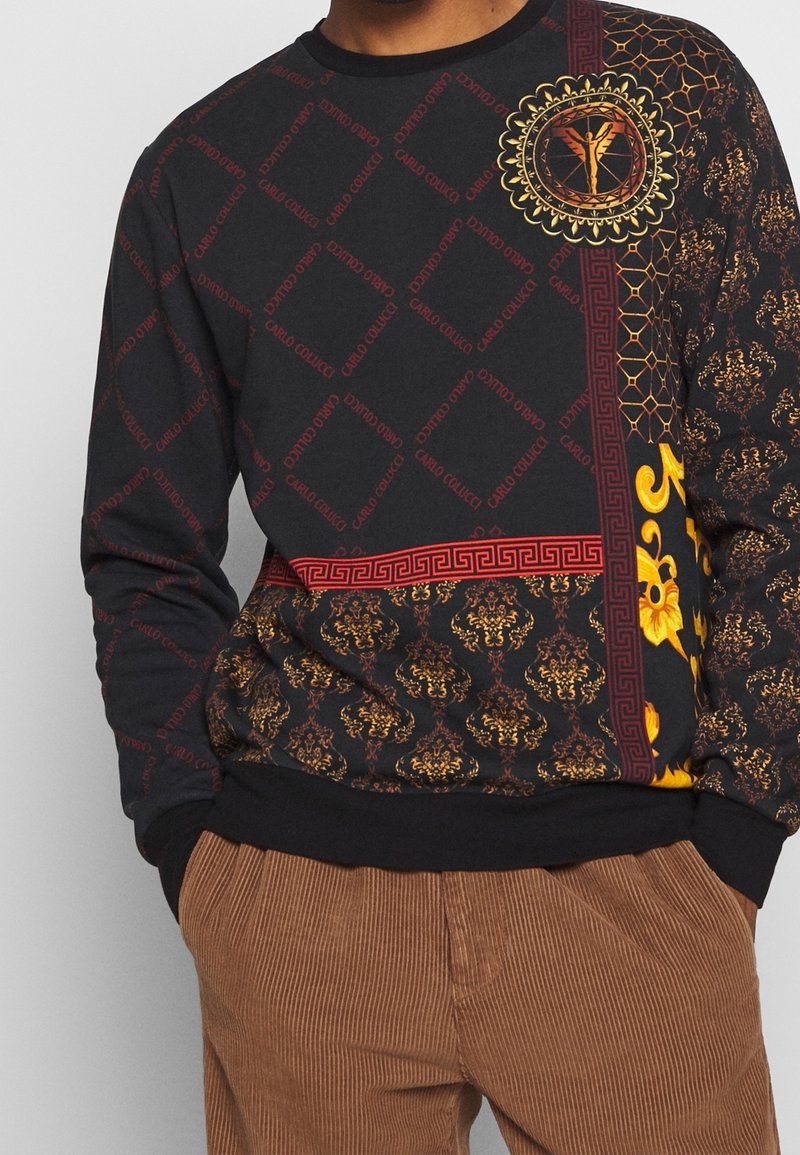 Sort sweatshirt med blandede mønstre: rød tekst, gyldne blomsterdesign og geometriske detaljer; ribbede manchetter og kant.