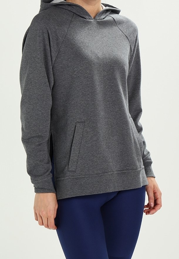 Personne portant un sweat à capuche gris à manches longues et des leggings bleu marine, debout devant un fond clair uni.