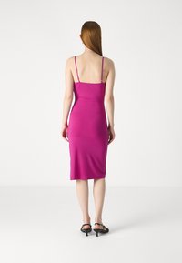 Robe midi ajustée en fuchsia vibrant, dotée de fines bretelles réglables et d'un tissu lisse et extensible qui épouser la silhouette.
