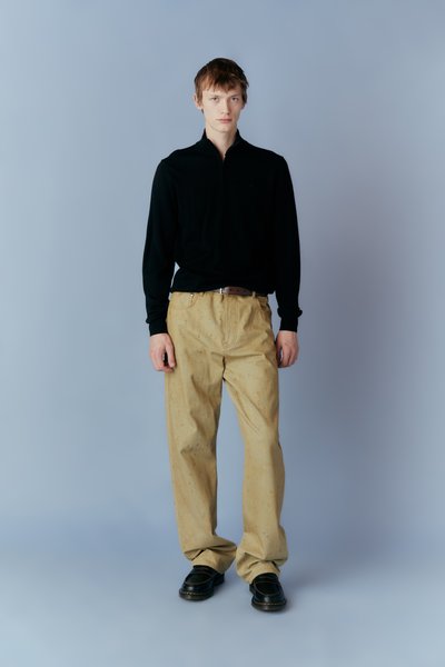 Μαύρο ζακέτα με φερμουάρ, μπεζ παντελόνια χαλαρής εφαρμογής και μαύρα παπούτσια. Απλός σχεδιασμός, μαλακή υφή και ουδέτερη παλέτα χρωμάτων.