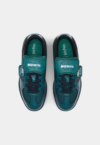 Zapatillas verdes y negras con parte superior de cuero liso, cierre de cordones y lengüeta acolchada con la marca "Slytherin". Plantilla texturizada.