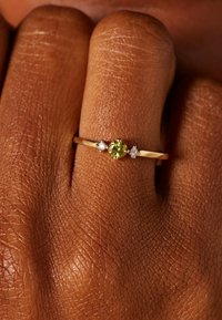 Gouden ring met een ronde groene edelsteen in het midden, omringd door twee kleine witte diamanten. Glad band met een gepolijste afwerking.