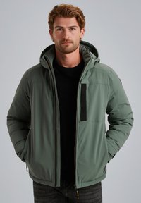 Giacca a vento verde con cappuccio, dotata di chiusura con zip e tasche laterali. Texture liscia, polsini regolabili e logo sul petto.