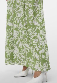 Zelené květinové maxi šaty s bílými vzory, vyrobené z lehké tkaniny. Spárováno s bílými texturovanými lodičkami na vysokém podpatku.