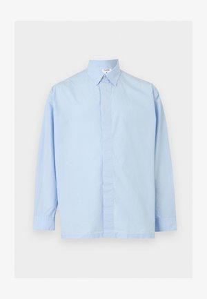 Vaaleansininen pitkähiha-painonappipaita klassisella kauluksella, piilotetulla nappilistalla ja kauluksessa näkyvällä merkinnällä.