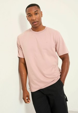 Light pink short-sleeved t-shirt with a round neckline, made of smooth fabric, featuring a subtle logo on the chest and relaxed fit.