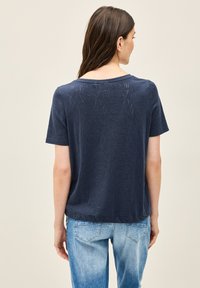 Navyblå kortærmet top med et struktureret bladmønster; rund halsudskæring og afslappet pasform, parret med lyseblå denimjeans.