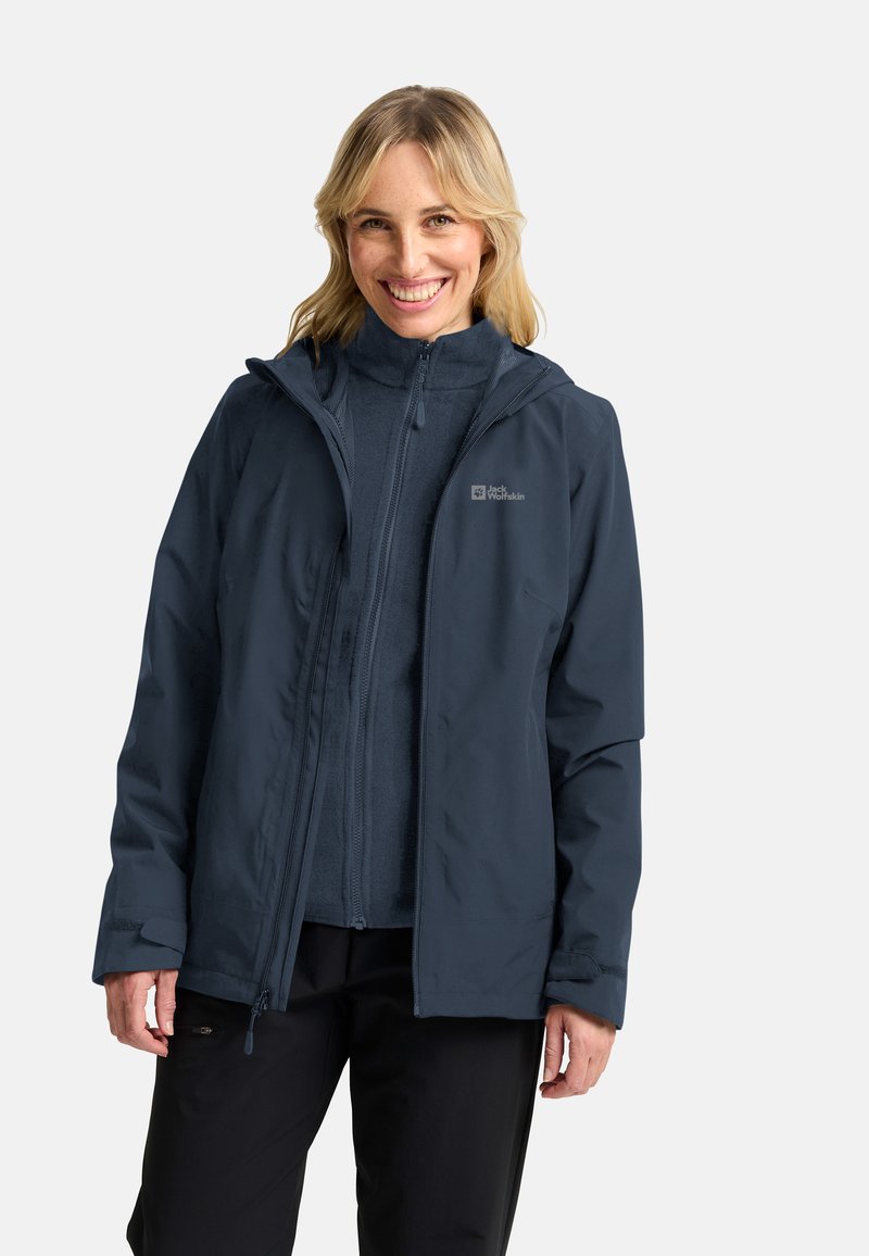 Giacca impermeabile blu navy con apertura a zip, cappuccio regolabile e morbida fodera interna. Abbinata a pantaloni scuri, con un logo sul petto.