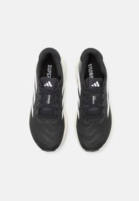 Black athletic shoes with a mesh upper, textured design, white midsole, and three white stripes on each side. Laces are black.