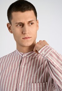 Camicia abbottonata con strisce verticali rosa e bianche, colletto a banda, maniche lunghe e taschino sul petto. Tessuto morbido e strutturato.