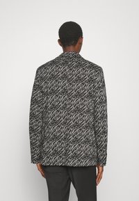 Blazer a righe bianco e nero con un design testurizzato, caratterizzato da maniche lunghe e una vestibilità personalizzata, mostrato da dietro.