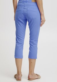 Modré zkrácené kalhoty vyrobené z hladkého materiálu, s dvěma zadními kapsami, ohrnutými manžetami a přiléhavým pasem. Navrženy pro ležérní vzhled.