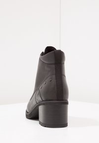 Botín de cuero negro hasta el tobillo con un tacón bajo, paneles laterales elásticos y costuras decorativas a lo largo de los lados. Textura suave con un diseño minimalista.