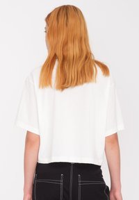 Camiseta blanca corta de tela suave con mangas cortas y dobladillo recto, combinada con pantalones negros de cintura alta con costuras blancas.