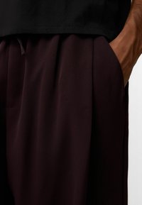 Mörk vinröda byxor med en slät textur, med veck och sidofickor. En svart t-shirt är delvis synlig ovanför midjan.