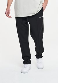 Schwarze Jogginghose aus weichem Stoff, mit elastischem Bund, Kordelzügen und Seitentaschen. Logodetail an der Hüfte.